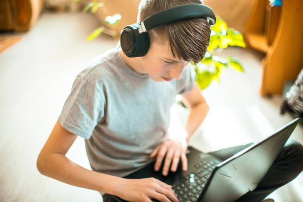 Teini-ikäinen hammasraudoissa, istuu läppärissä lattialla. poika muodikas sisustus lähellä trendikkäitä vihreitä kasveja talvipuutarhasta opettaa opetuksia verkossa kotona - Valokuva, kuva