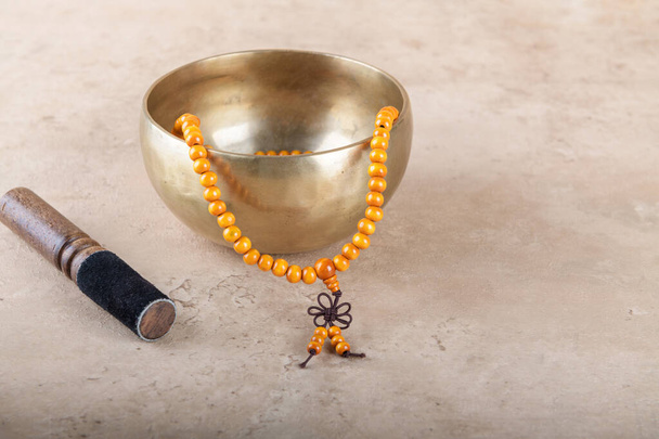 Tibetská pěvecká mísa s tyčinkou, malými perleťovými prameny používanými při mantrických meditacích na béžovém kamenném pozadí. Zvukové léčebné hudební nástroje pro meditaci, relaxaci, jógu, masáž, duševní zdraví - Fotografie, Obrázek