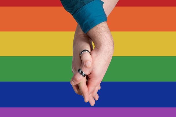 Homosexuelles Paar reicht sich auf Regenbogenfahne die Hände - Foto, Bild