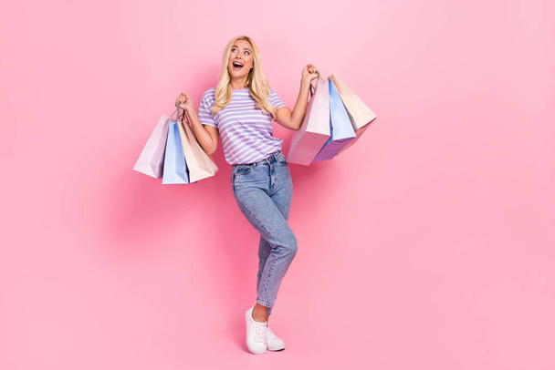 Full size portrait of positive cheerful girl hold packages look empty space isolated on pink color background. - Фото, зображення