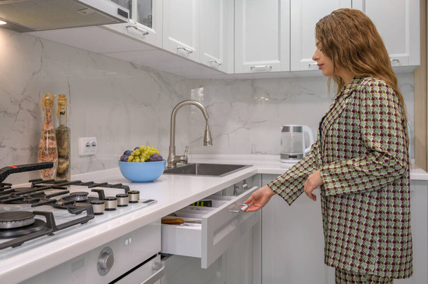 Lindo ama de casa joven saca el cajón del gabinete en la cocina gris claro - Foto, Imagen