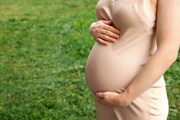 Pregnant woman touching belly on green grass, closeup. Space for text - Valokuva, kuva