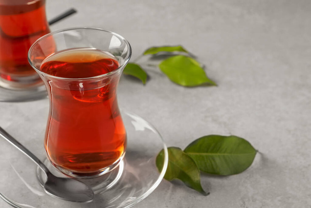 Glasses with traditional Turkish tea and green leaves on light grey table, closeup. Space for text - Foto, Bild