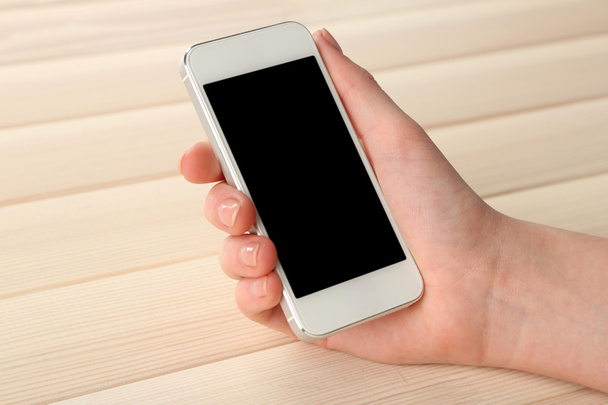 Mão usando telefone celular inteligente no fundo da mesa de madeira
 - Foto, Imagem