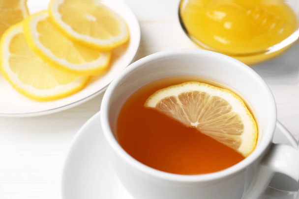 Cup with delicious immunity boosting tea, lemon and honey on white wooden table, closeup - Фото, изображение