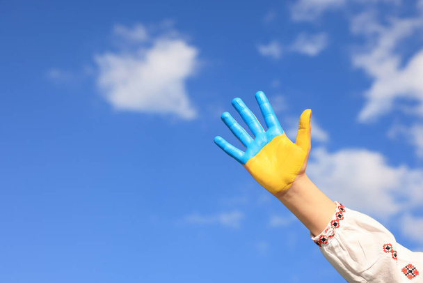 Little girl with hand painted in Ukrainian flag colors against blue sky, closeup and space for text. Love Ukraine concept - Φωτογραφία, εικόνα