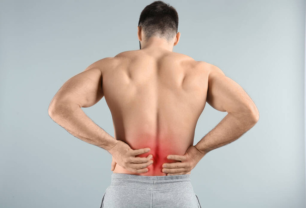 Young man suffering from back pain on light background - Fotó, kép