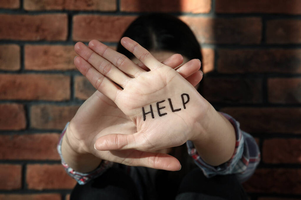 Domestic violence concept. Woman hiding her face, focus on hands with written word Help - Fotó, kép