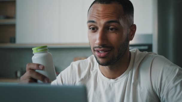 Homme nutritionniste africain homme en ligne Fitness formateur vidéoconférence avec ordinateur portable dans la cuisine parler de pilules protéines vitamines commerce en ligne vente compléments alimentaires fitness nutrition pot - Séquence, vidéo