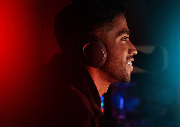 Headphones, gaming and neon with a man streamer playing a video game online for a subscription service. Gamer, streaming and esports with a male geek or nerd enjoying computer games in a mancave. - Photo, Image