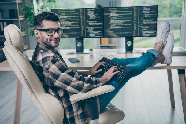 Full body profile portrait of intelligent positive web designer man sit chair put legs table keyboard typing open space indoors. - 写真・画像