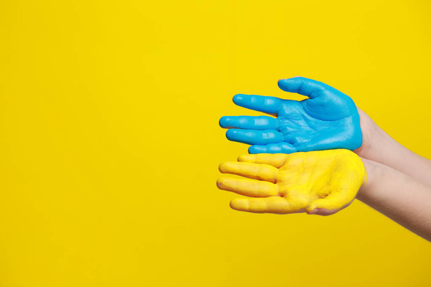Little boy with hands painted in Ukrainian flag colors on yellow background, closeup and space for text. Love Ukraine concept - Foto, afbeelding