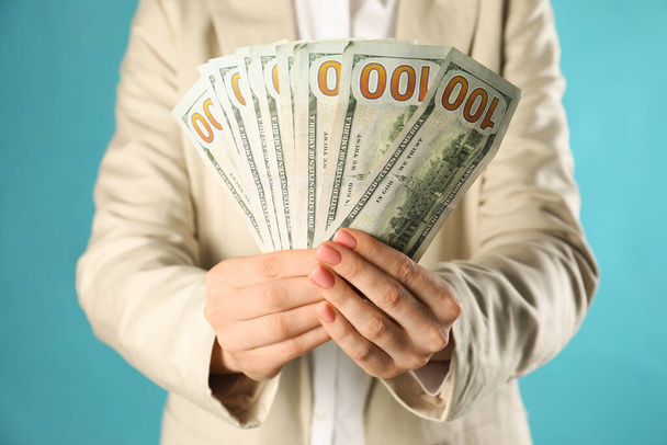Woman holding dollar banknotes on turquoise background, closeup. Money exchange concept - Foto, Bild