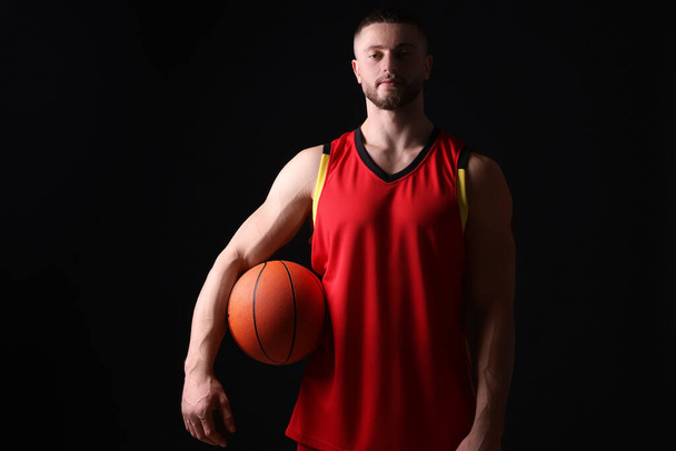 Athletic young man with basketball ball on black background - Фото, изображение