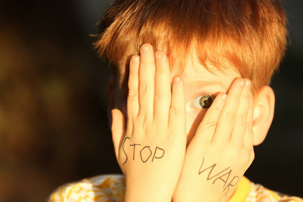 Little boy hiding face and words Stop War written on his hands outdoors, closeup - Φωτογραφία, εικόνα