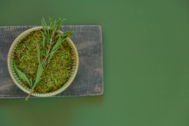 Stevia rebaudiana. Getrocknetes Stevia und grüner Zweig in einer runden Tasse auf einem Holzbrett auf dunklem olivem Hintergrund. Zuckerersatz. Natürliche Süßstoffe. - Foto, Bild