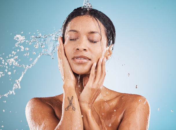 Wasser, Reinigung und Dusche mit einer schwarzen Frau im Studio auf blauem Hintergrund für Hygiene oder Hydratation. Entspannen, Hautpflege und Wellness mit einer attraktiven jungen Frau, die ihre Haut im Badezimmer wäscht. - Foto, Bild