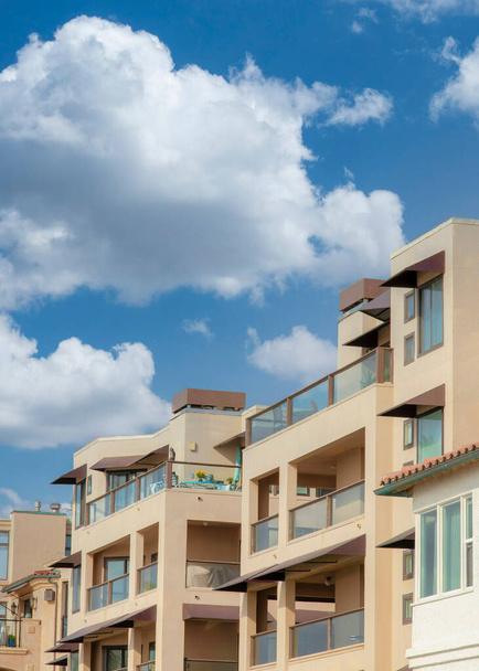 Vertical Nubes hinchadas blancas Edificios residenciales con barandillas de vidrio en La Jolla, California. Exterior de edificios de barrio con diferentes diseños contra el cielo gris claro. - Foto, imagen