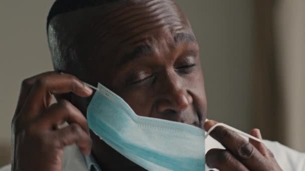 Опытный африканский врач-этнотерапевт, глядя в камеру, надевает маску, покрывает рот, нос использует индивидуальный защитный респиратор от коронавируса ковида-19, чтобы остановить вспышку пандемии - Кадры, видео