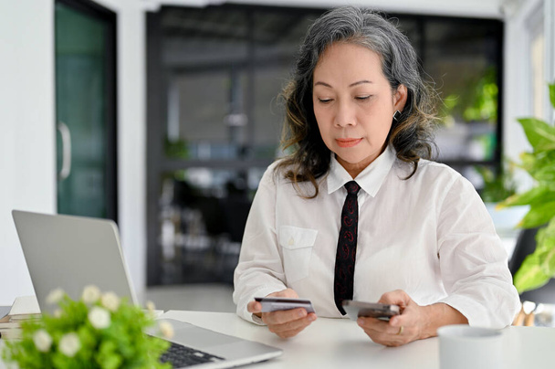 Professionnel asiatique femme d'affaires âgée en utilisant son smartphone pour payer des factures en ligne ou transférer de l'argent. - Photo, image