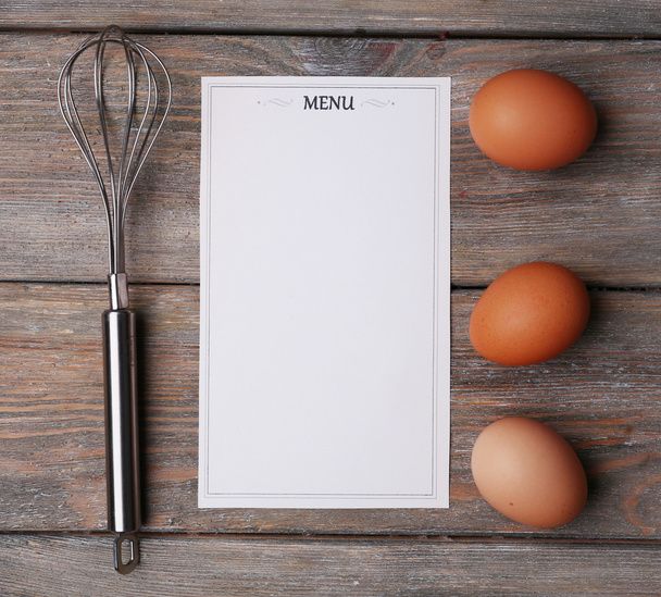 Menu sheet of paper with egg whisk and eggs on rustic wooden surface background - Foto, Bild
