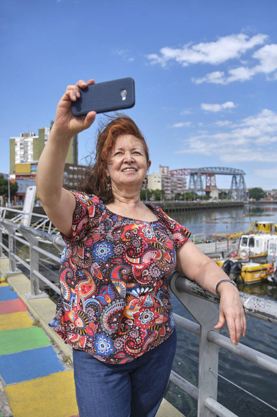 Female tourist taking a self portrait with her smartphone in the touristic neighborhood of La Boca, in Buenos Aires, Argentina, on a sunny summer day. - Photo, Image