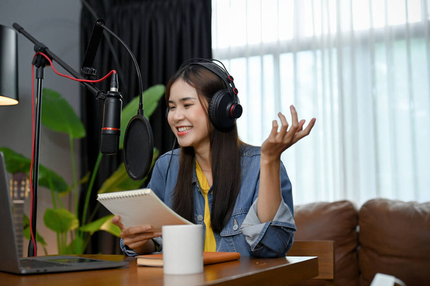 Cheerful and happy young Asian female radio host or online influencer is recording and board-casting her online radio channel in her home studio. freelance content creator concept. - Photo, Image