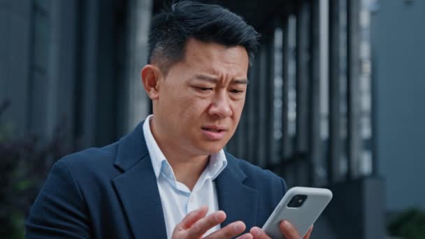 Mad stressato asiatico di mezza età 40 uomo leader uomo d'affari in possesso di cellulare all'aperto infastidito con l'errore di app mobile messaggio di spam in piedi in città sconvolto da lento problema di connessione smartphone rotto - Filmati, video