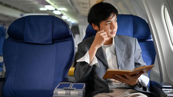 Розумний і професійний азіатський бізнесмен або менеджер чоловічої статі в літаку, сидить в бізнес-класі, думаючи і плануючи свій бізнес, дивлячись у вікно. - Фото, зображення