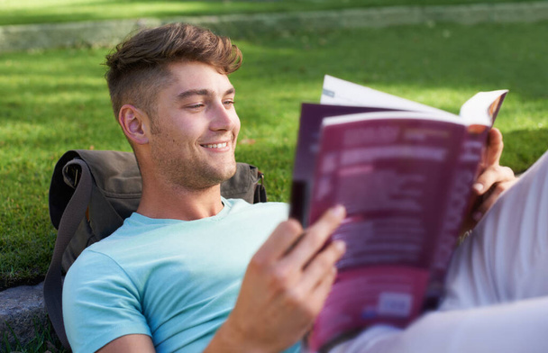 O okuduğu şeyi seviyor. Parkta uzanmış ders kitabı okuyan genç bir adam. - Fotoğraf, Görsel