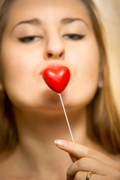 όμορφη νέα γυναίκα που κρατά διακοσμητική κόκκινη καρδιά στα χείλη - Φωτογραφία, εικόνα