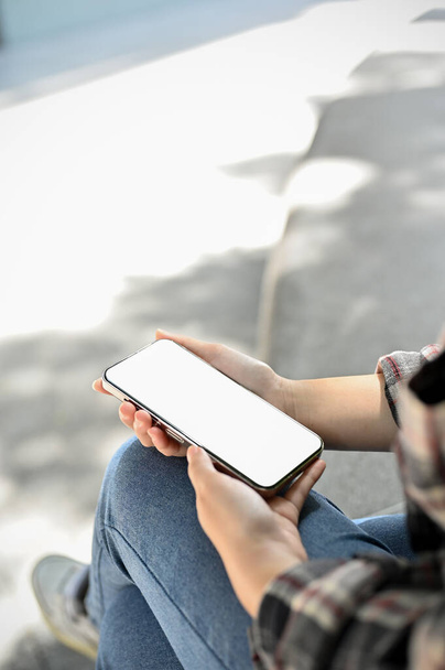 Una joven asiática usando su smartphone mientras se relaja en el parque de la ciudad. mockup de pantalla blanca del teléfono móvil. imagen de primer plano - Foto, imagen