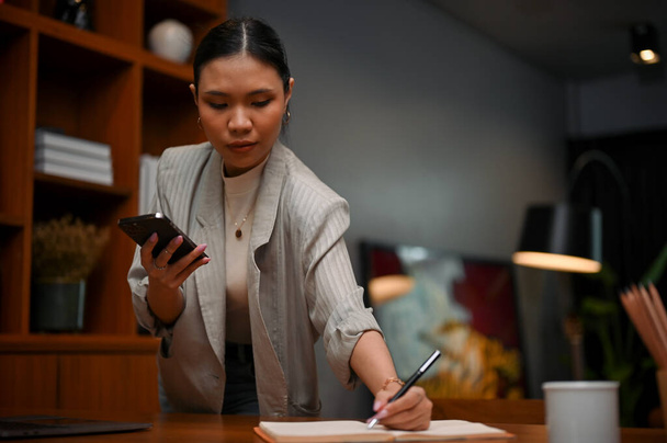 Profesional millennial Asiática mujer jefe o mujer de negocios se concentró en sus tareas de negocios, la planificación de su agenda de reuniones y tomar notas en su cuaderno. - Foto, Imagen