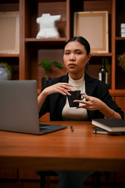 Porträt: Elegante und selbstbewusste asiatische Geschäftsfrau mit einer Tasse Kaffee an ihrem Schreibtisch in ihrem privaten Büro. - Foto, Bild