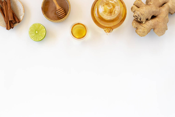 Vista superior de una taza de té con raíz de jengibre, lima, canela y tetera sobre fondo blanco. Concepto de bebida saludable. - Foto, imagen