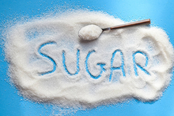 Kaşık ve mavi arka planda şeker, yiyecek için beyaz şeker ve tatlı şeker yığını şeker kristal granüle - üst görünüm  - Fotoğraf, Görsel