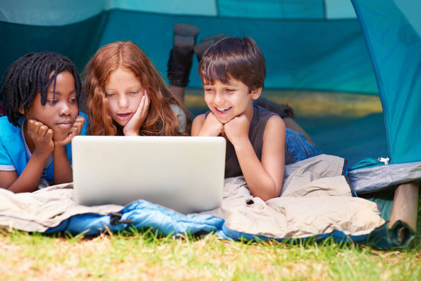 Always connected, no matter where they are - Modern technology. Children enjoying watching something on a laptop while out camping in a tent - Foto, Imagen