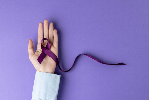 Hand holding purple ribbon on purple background with copy space. Medicine, healthcare and science concept. - Foto, Bild