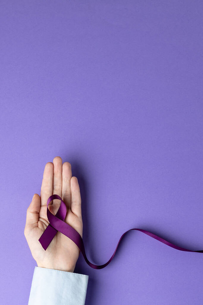Hand holding purple ribbon on purple background with copy space. Medicine, healthcare and science concept. - Fotoğraf, Görsel