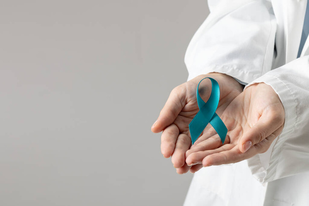 Midsection of caucasian doctor holding blue ribbon on grey background with copy space. Medicine, healthcare and science concept. - Valokuva, kuva