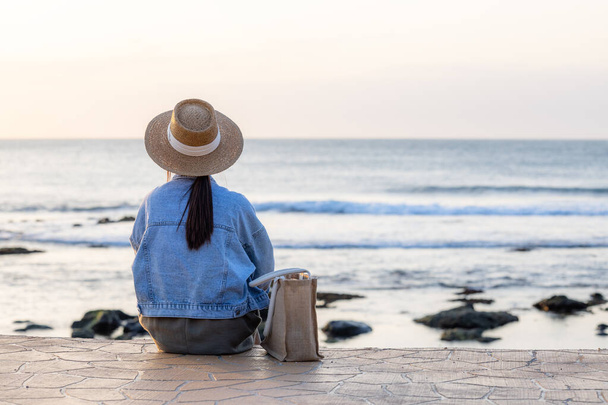 Turystka siedzi nad morzem pod zachodem słońca - Zdjęcie, obraz