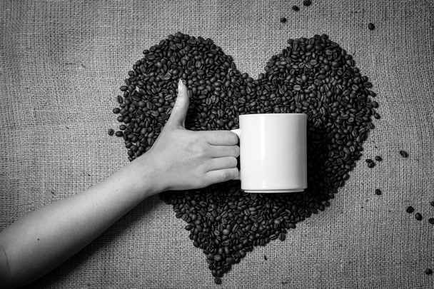 Mano con pollice in su tenendo tazza contro cuore fatto di chicco di caffè
 - Foto, immagini