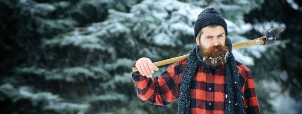 Hipster with beard on serious face with axe. Lumberjack brutal bearded man holds axe. Brutal lumberjack in winter. Lumberjack hipster in snowy forest - Zdjęcie, obraz