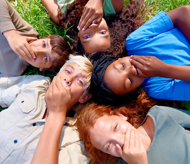 ¿Puedes guardar un secreto? Un grupo de niños tumbados en la hierba cubriéndose la boca - Foto, Imagen