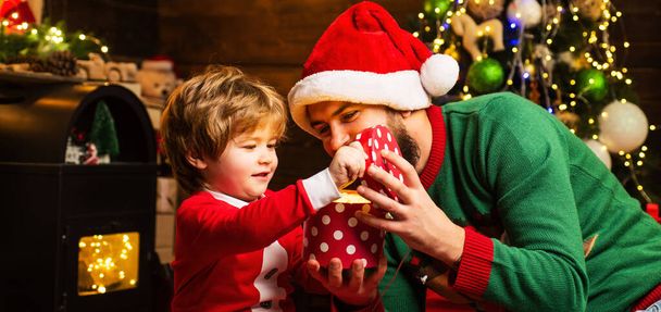 Daddy and son open Christmas gift. Father and son Wish you merry Christmas. Happy father and son in Santa hat with present have a Christmas at home - Fotó, kép