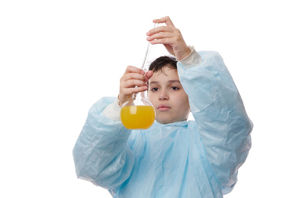 Pipeti laboratuvar matarasından sarı kimyasal sıvıyla dolduran, reaktörü düşüren ve bilim okulu laboratuarında bir kimya deneyi yapan genç bir çocuğun ellerine odaklan. - Fotoğraf, Görsel