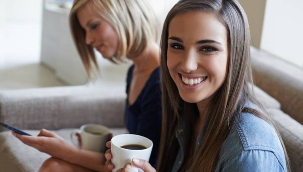 Catching up over a cup of coffee. Two young woman smiling as they drink coffee on a couch - Zdjęcie, obraz