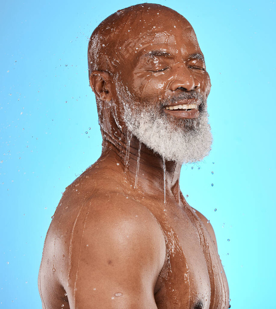 Studio, eau et vieil homme dans une douche nettoyant son visage ou son corps pour des soins de beauté ou de bien-être sur fond bleu. Sourire, sain ou heureux vieux mannequin homme lavage ou détente avec maquette espace. - Photo, image