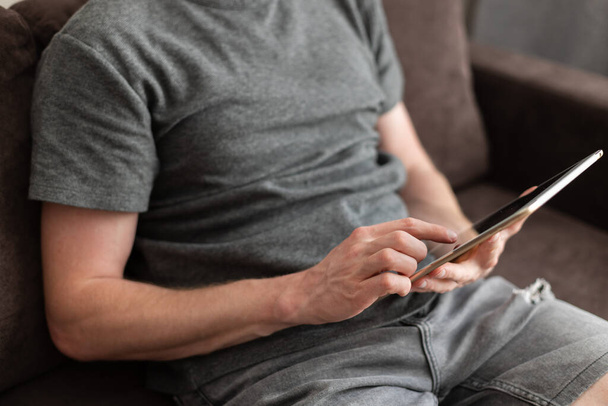 Un uomo seduto su un divano con un tablet in mano. Utilizzo della tecnologia - Foto, immagini