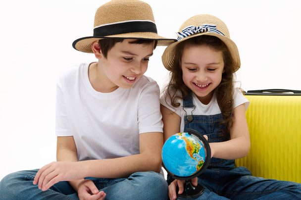 Многонациональные дети, мальчик и девочка с чемоданом, брат и сестра, отправляющиеся на летние каникулы, указывающие пальцем на место на глобусе с картой Земли, выбирающие новое туристическое направление для отдыха - Фото, изображение
